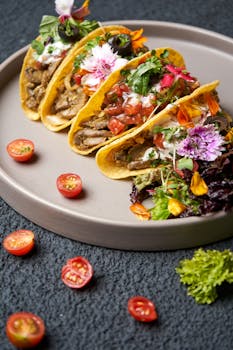 Close-up of gourmet tacos garnished with fresh herbs and edible flowers on a plate.