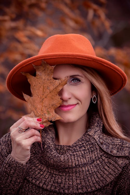 無料 乾燥した葉を保持しているオレンジ色の帽子をかぶっている女性 写真素材