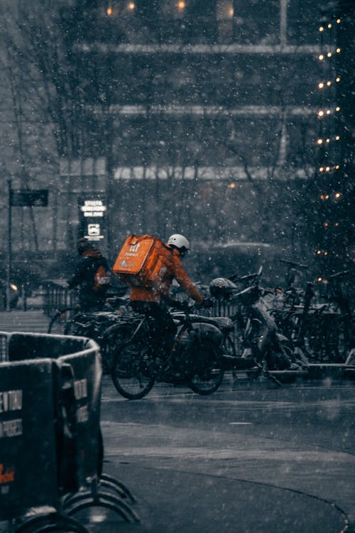 Food Delivery Man with a Backpack Riding on a Bicycle in City during a Snowfall 