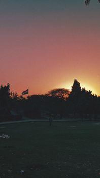 A serene sunset scene with the Indian flag silhouetted against vibrant skies, captured in a park in Delhi.