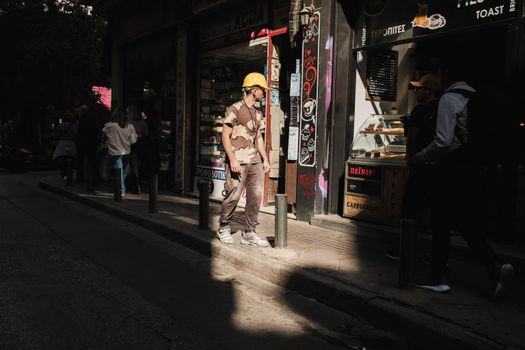 A busy street in Athens features a construction worker and passersby.