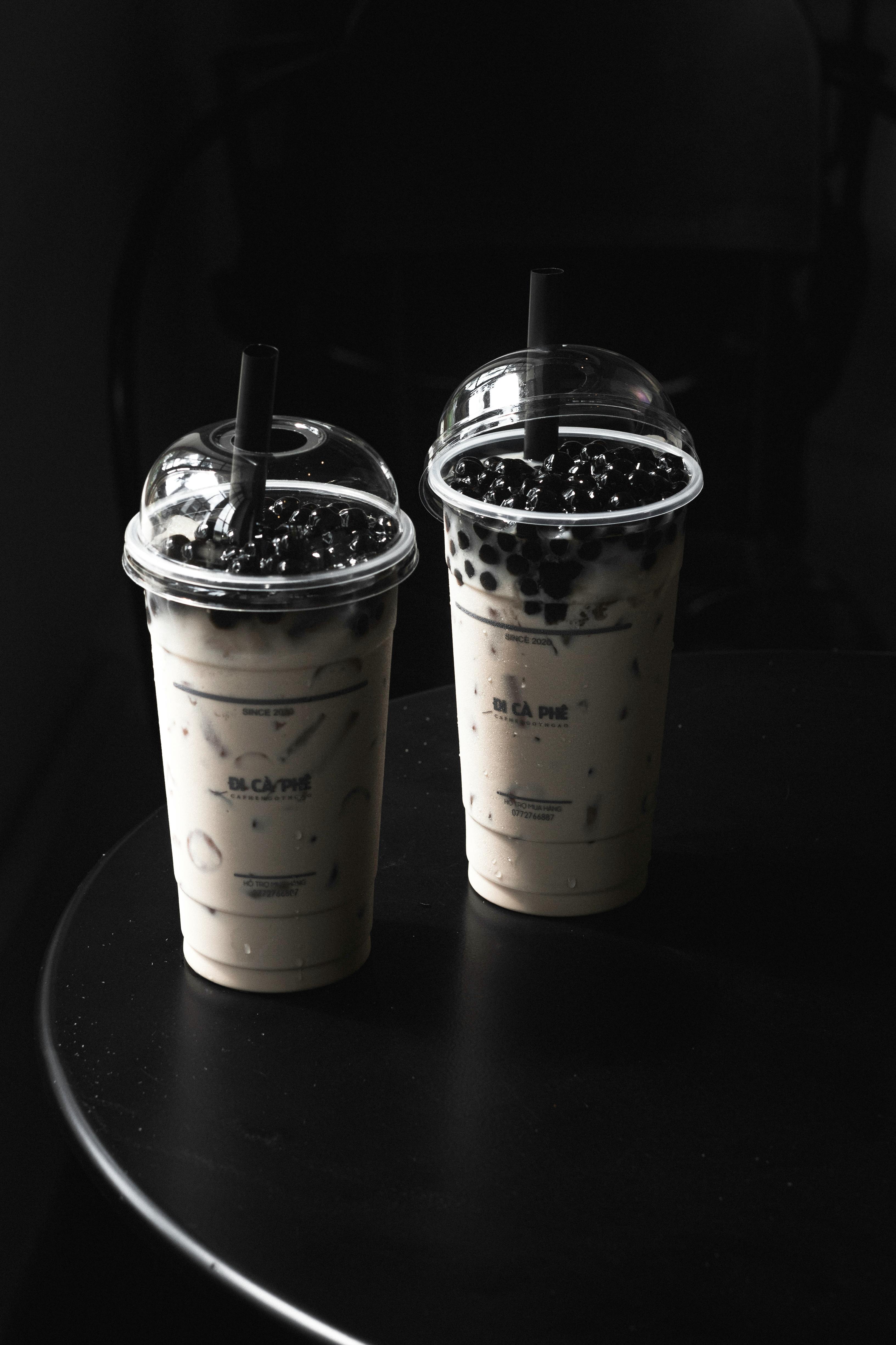Studio photo of two bubble tea cups with tapioca pearls, featuring moody lighting on a black background.
