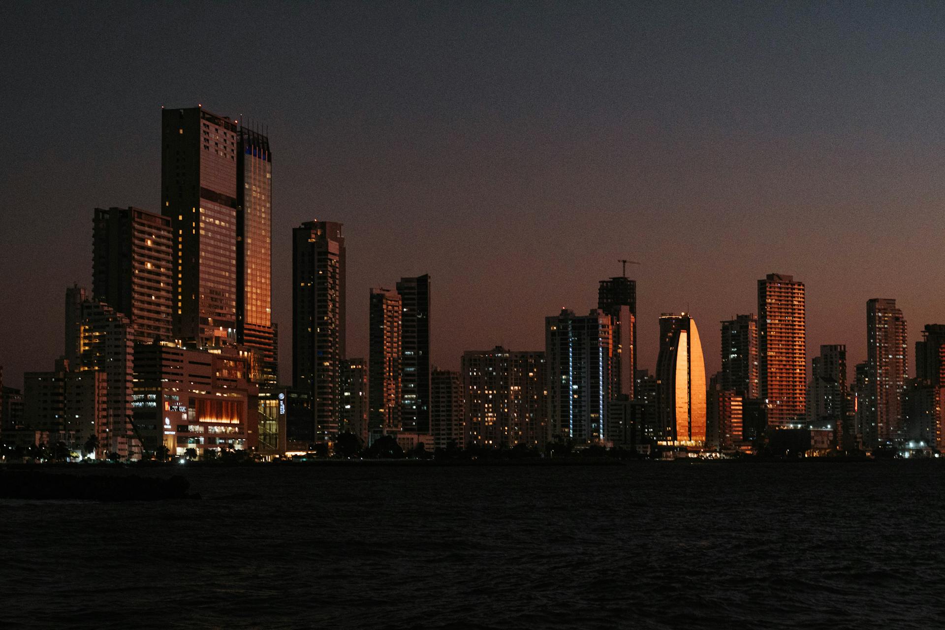 Explore the illuminated skyline of Cartagena de Indias against a serene dusk sky, featuring iconic skyscrapers.