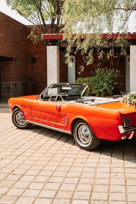 Red vintage convertible with flowers in a sunlit courtyard, perfect for weddings or luxury events.