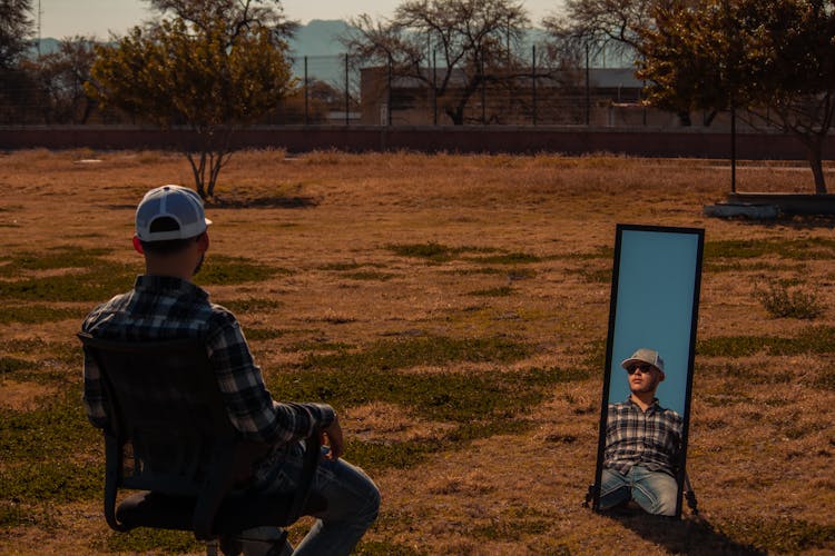 Man Sitting On Chair Reflecting In Mirror