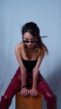 Young woman in trendy outfit sitting confidently, showcasing modern fashion style with red pants and sunglasses.