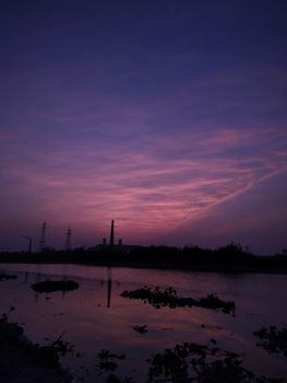 A peaceful dusk scene with a dramatic sky and industrial silhouette by a serene lake.