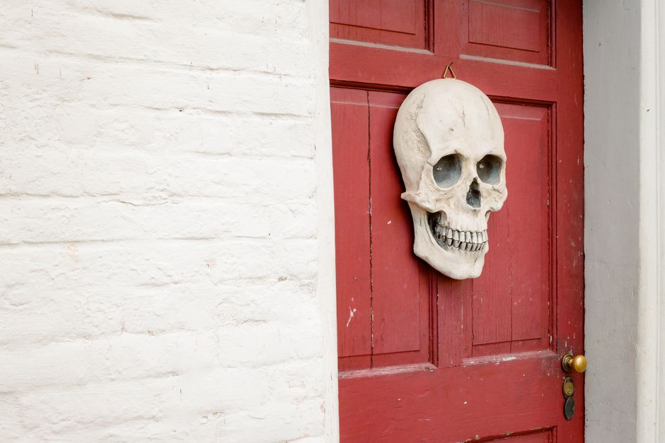 A skull decoration hanging on a red door, perfect for Halloween ambiance.