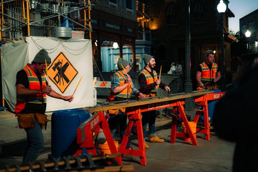Street performers in construction gear play music at an urban night scene.