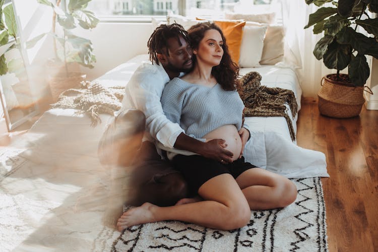 Man Sitting On Bedroom Floor Cradling Womans Belly