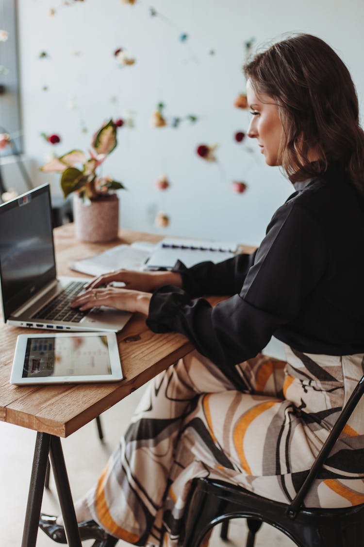 Woman Sitting By Desk Working On Laptop