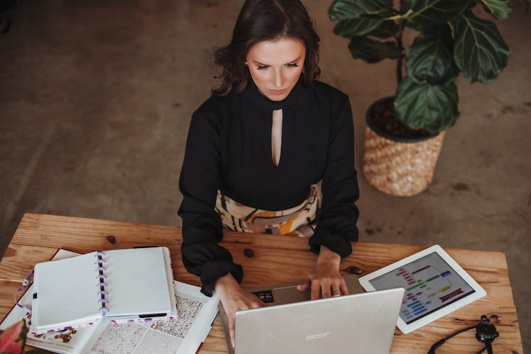 Woman Sitting By Wooden Desk Working On Laptop