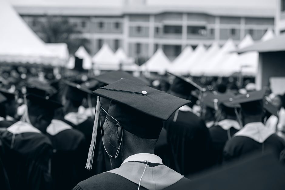 A black and white photo of students in caps and gowns at a university graduation ceremony outdoors.