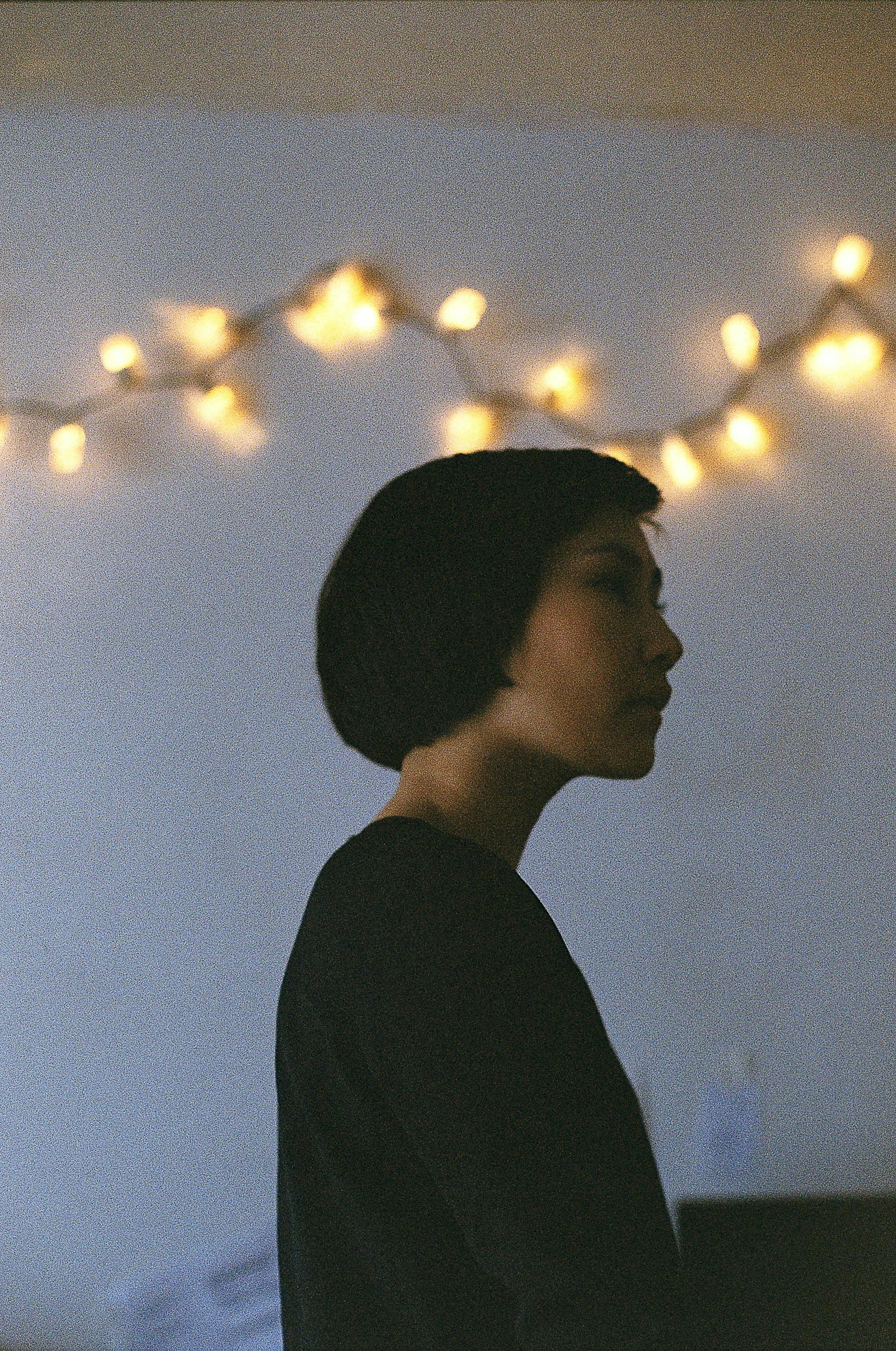 Artistic silhouette of a woman indoors, with warm string lights creating an ambient mood.