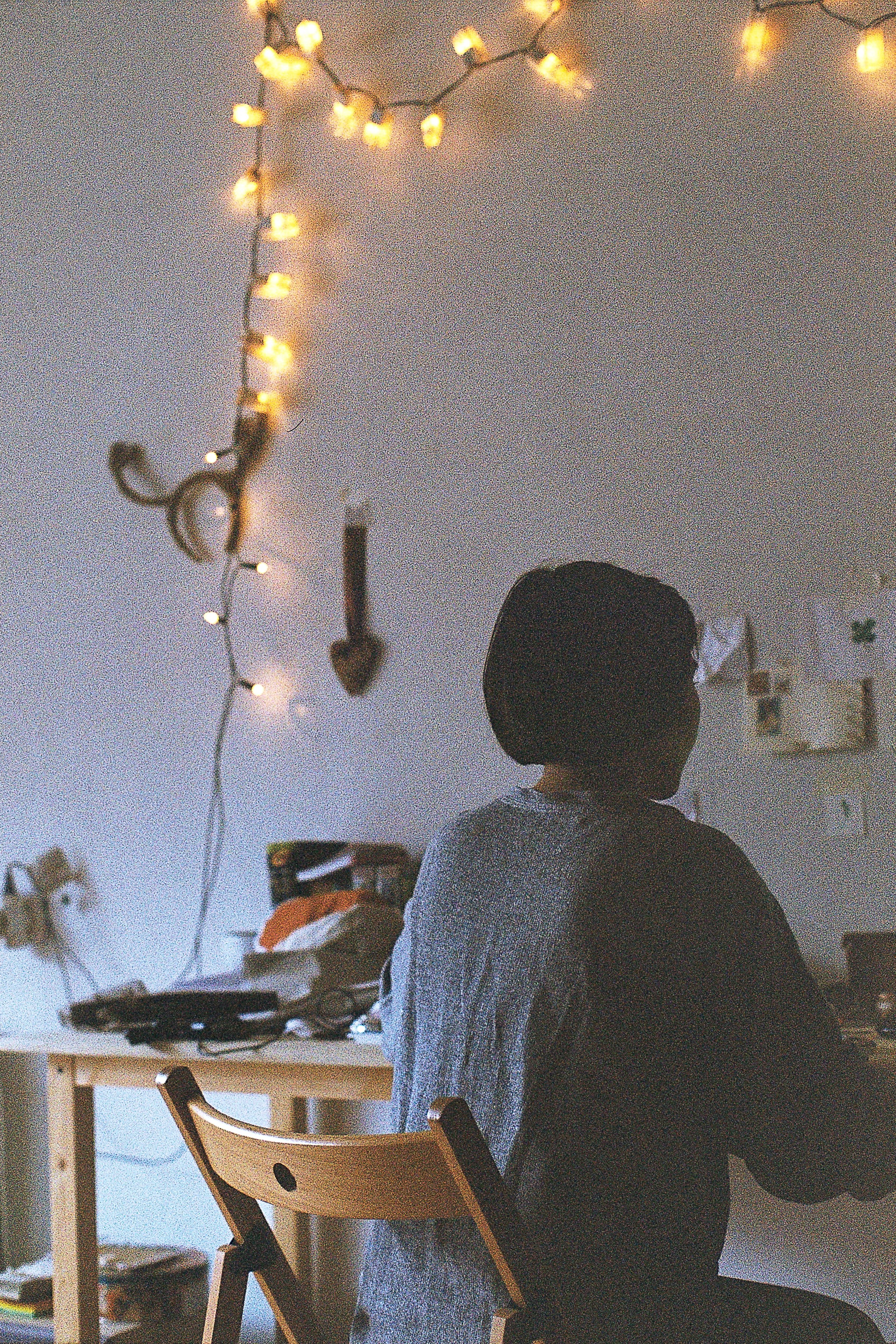 A cozy home office setup with warm string lights and a person working at a desk.
