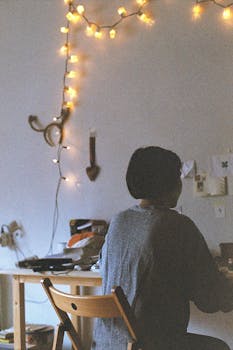 A cozy home office setup with warm string lights and a person working at a desk.