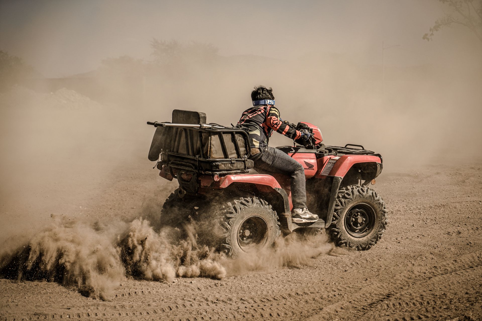 Thrilling action of an adult riding a quad bike through dust on an off-road trail.