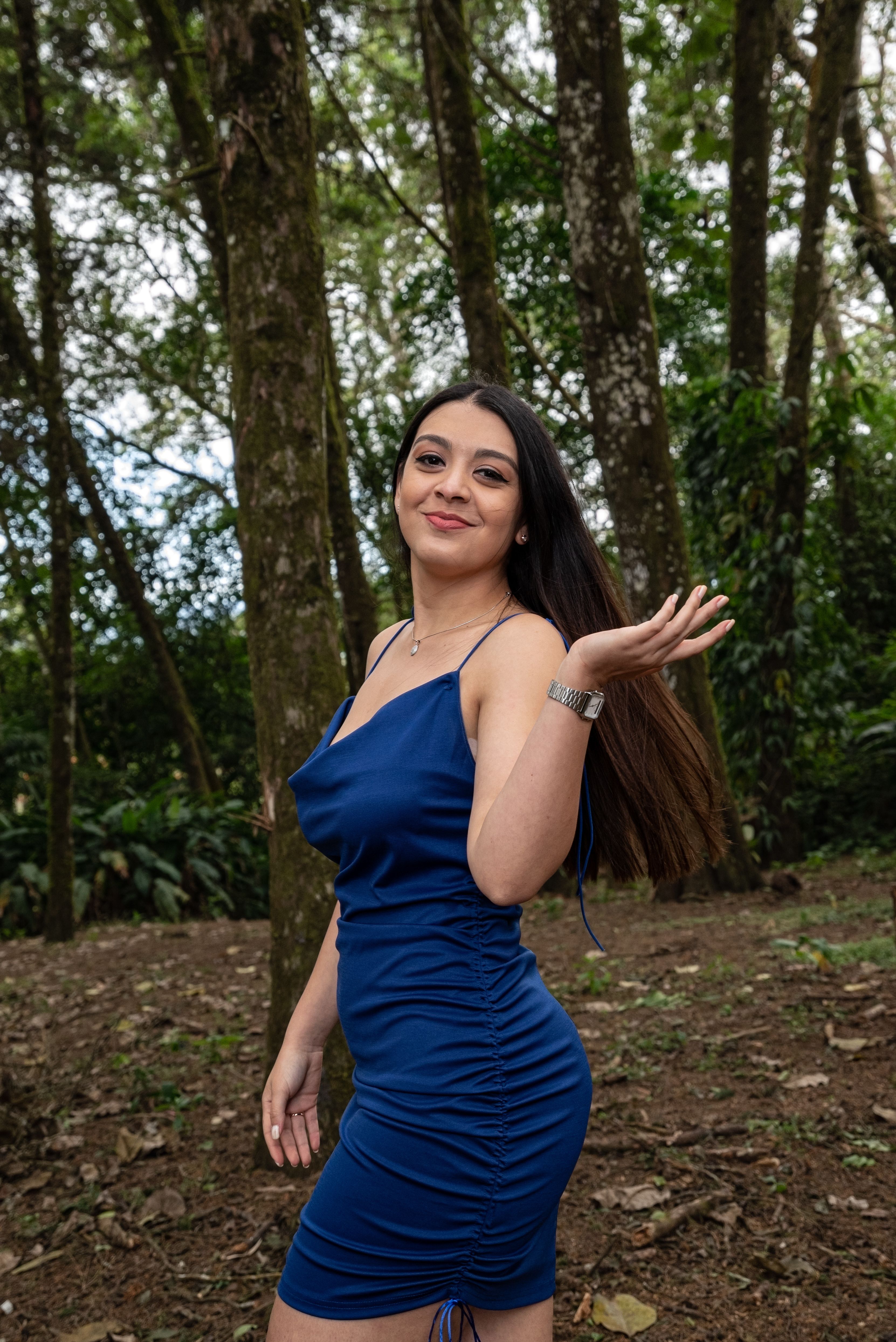 A young woman poses confidently in a blue dress amidst a lush Costa Rican forest.