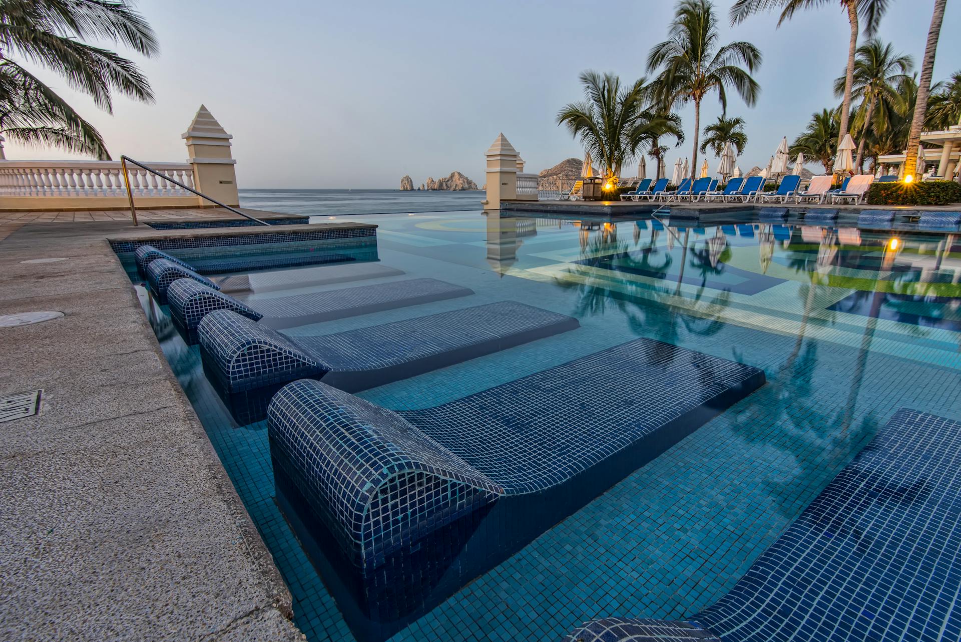 Serene poolside view overlooking the ocean with palm trees and lounge chairs in Cabo San Lucas, capturing tropical tranquility.