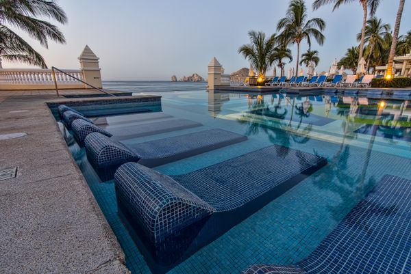 Blue sun loungers beside a serene outdoor swimming pool with ocean views on a sunny California summer day