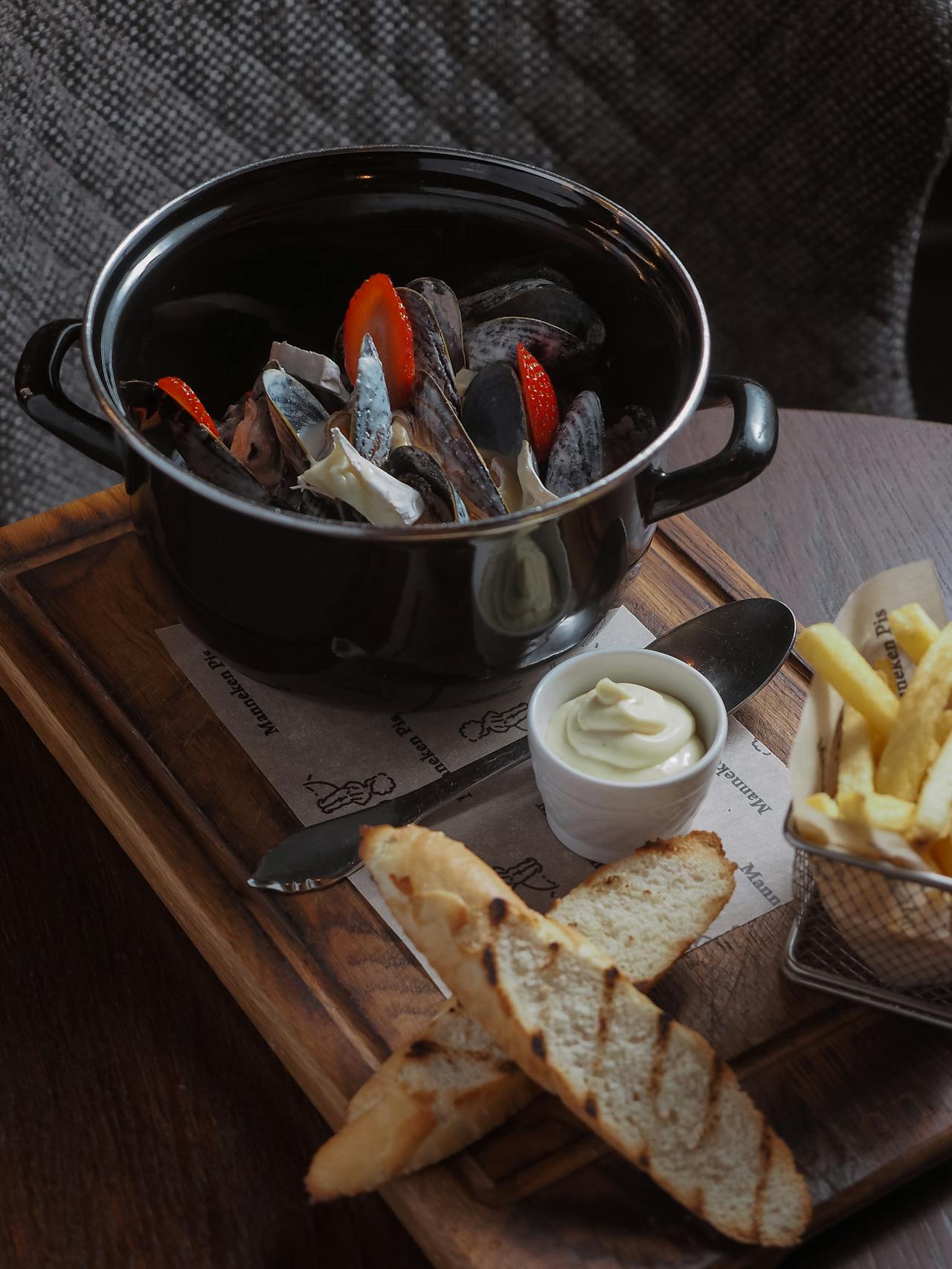 Pentola con cozze cotte e pane su tagliere di legno vicino ai fornelli