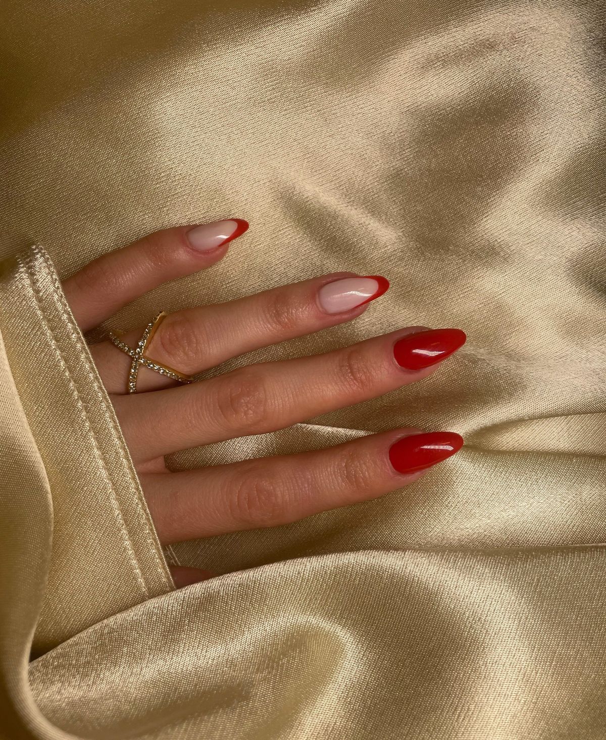 Close-up shot of a woman's hand with stunning red manicured nails resting on luxurious gold fabric.