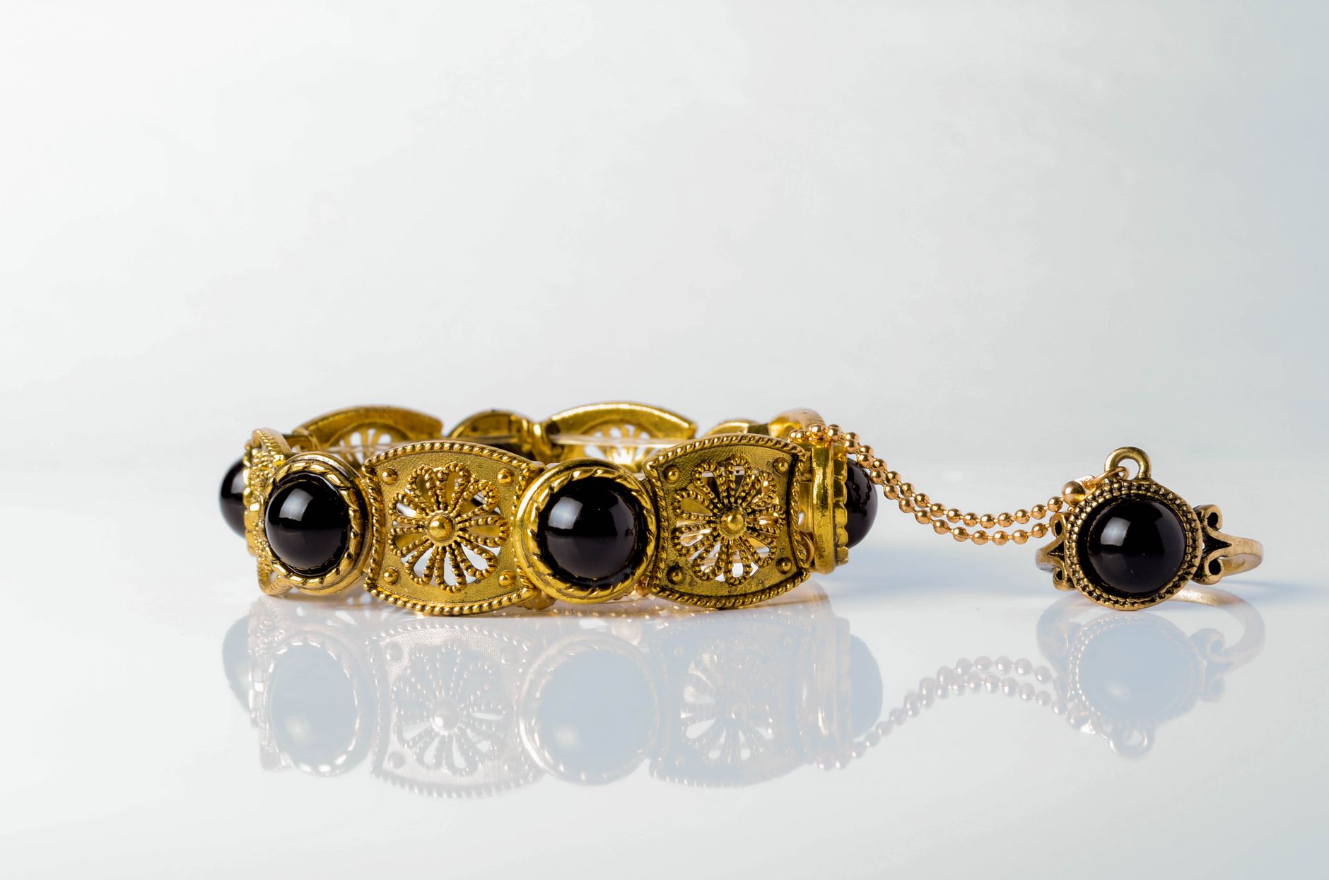 Close-up of an ornate gold bracelet with black onyx stones on a reflective white surface.