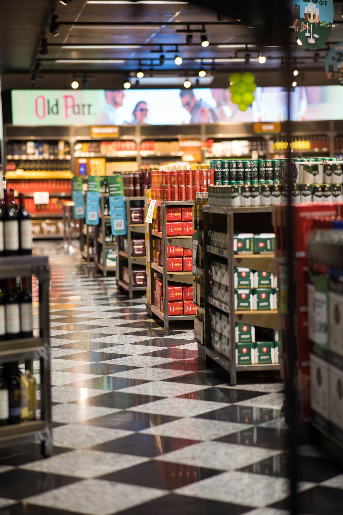 A bright, quiet supermarket aisle with neatly stacked shelves and an empty floor