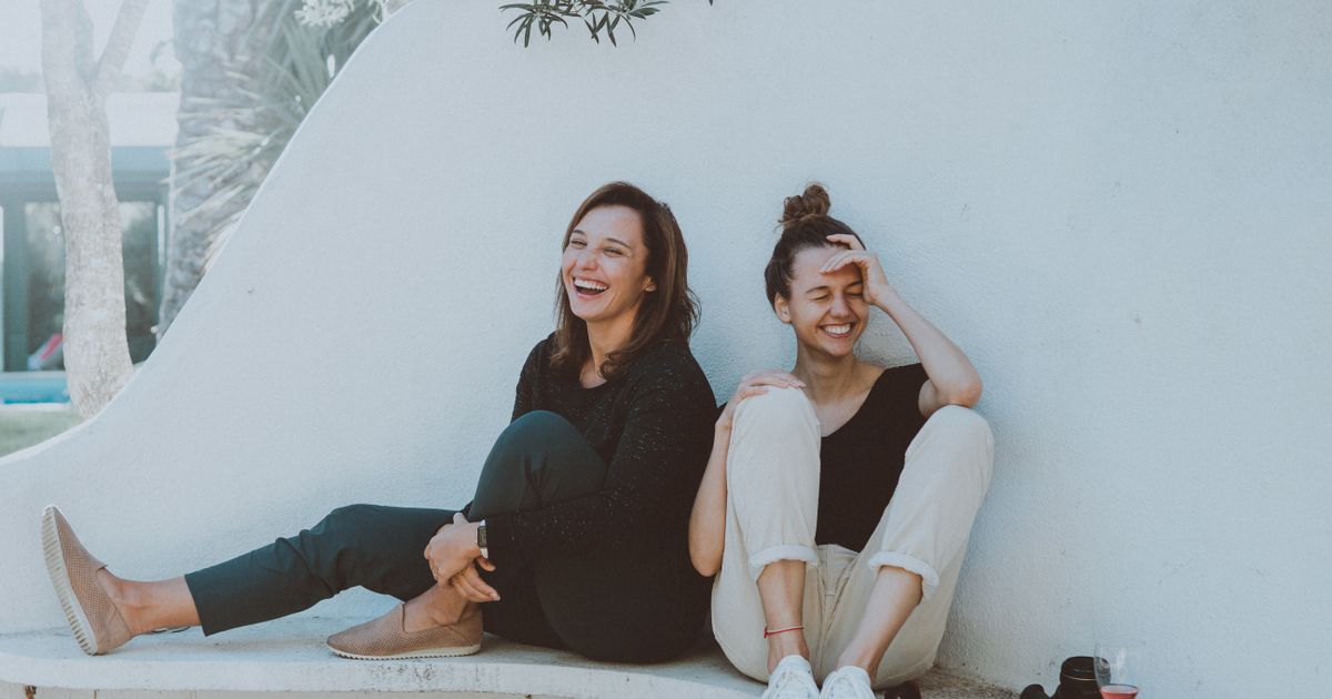 Two friends laughing together against a white wall