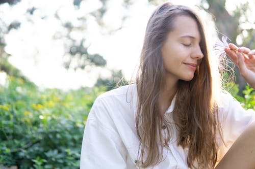 Woman Closing Her Eyes While Holding White Petaled Flower