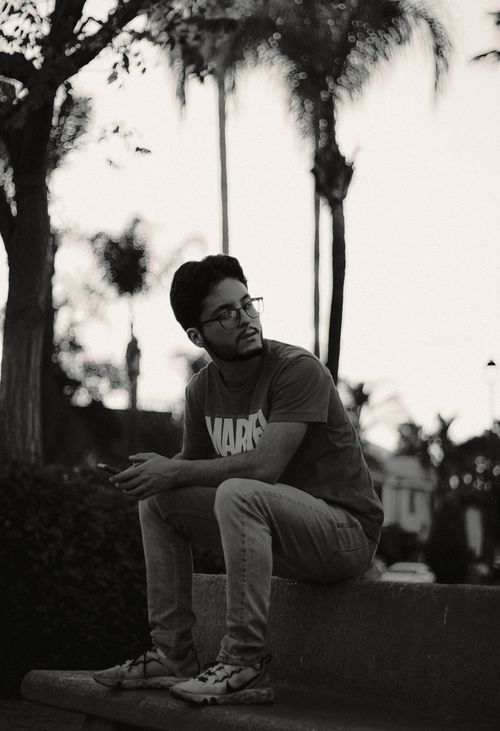 Free A man with glasses sits on a bench outdoors, captured in a contemplative pose in monochrome. Stock Photo