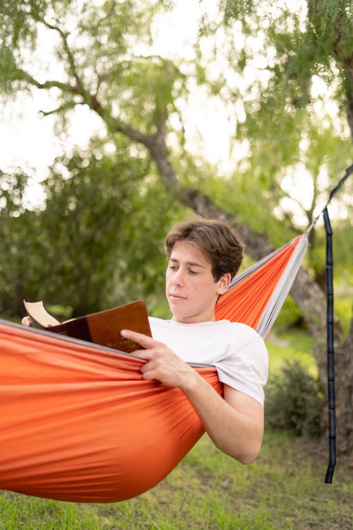 Man Lying Down on Hammock and Reading Book