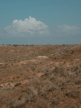 A wide shot of a dry desert landscape under a clear sky with clouds in the distance.