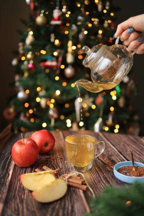 Free Warm apple cider being poured with a bokeh-lit Christmas tree in the background, creating a festive holiday vibe. Stock Photo