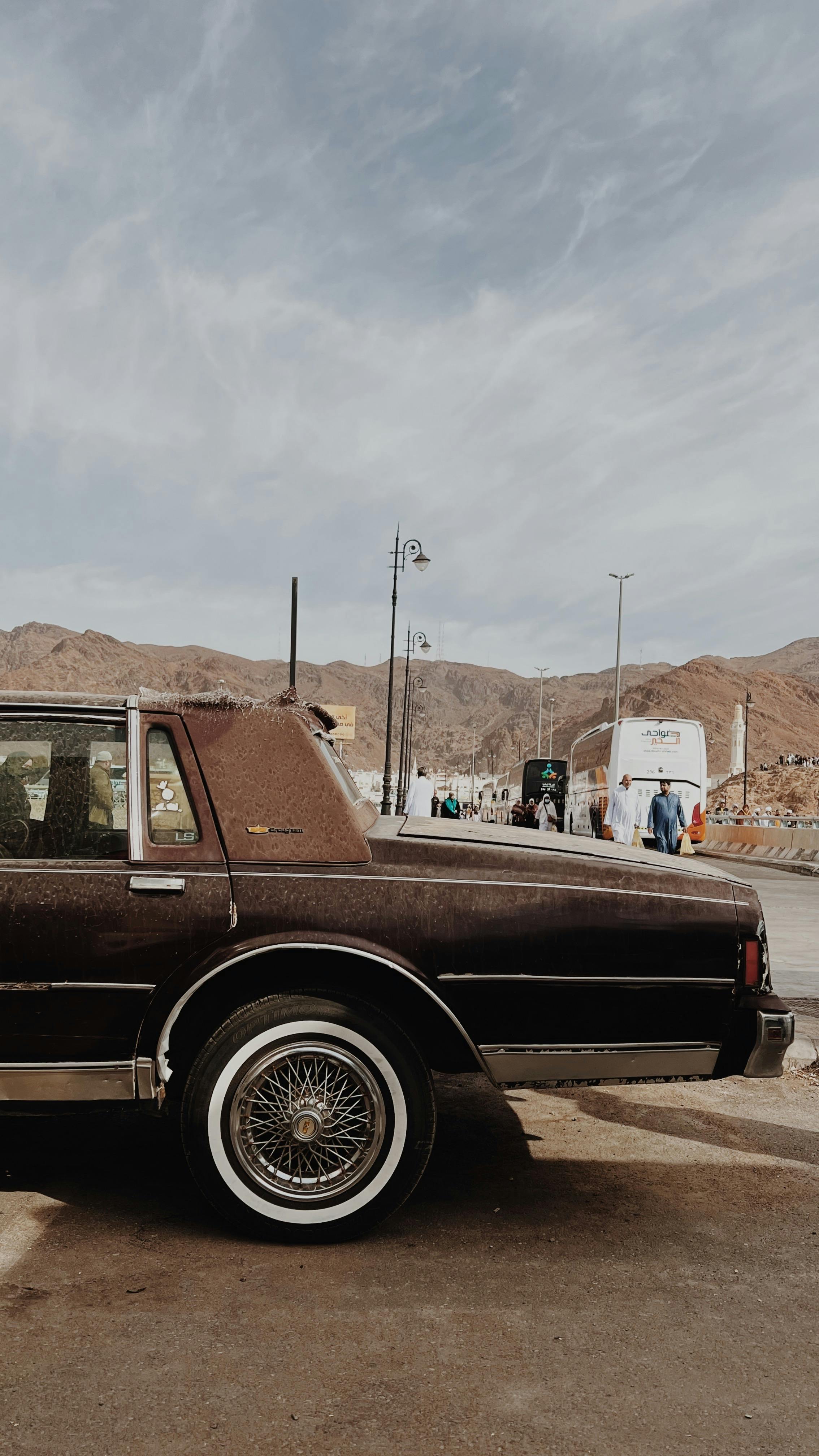 Classic car parked against a mountain backdrop under a bright sky.