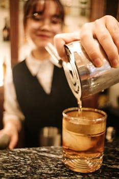A female bartender pouring an elegant cocktail with a smile at a stylish indoor bar.