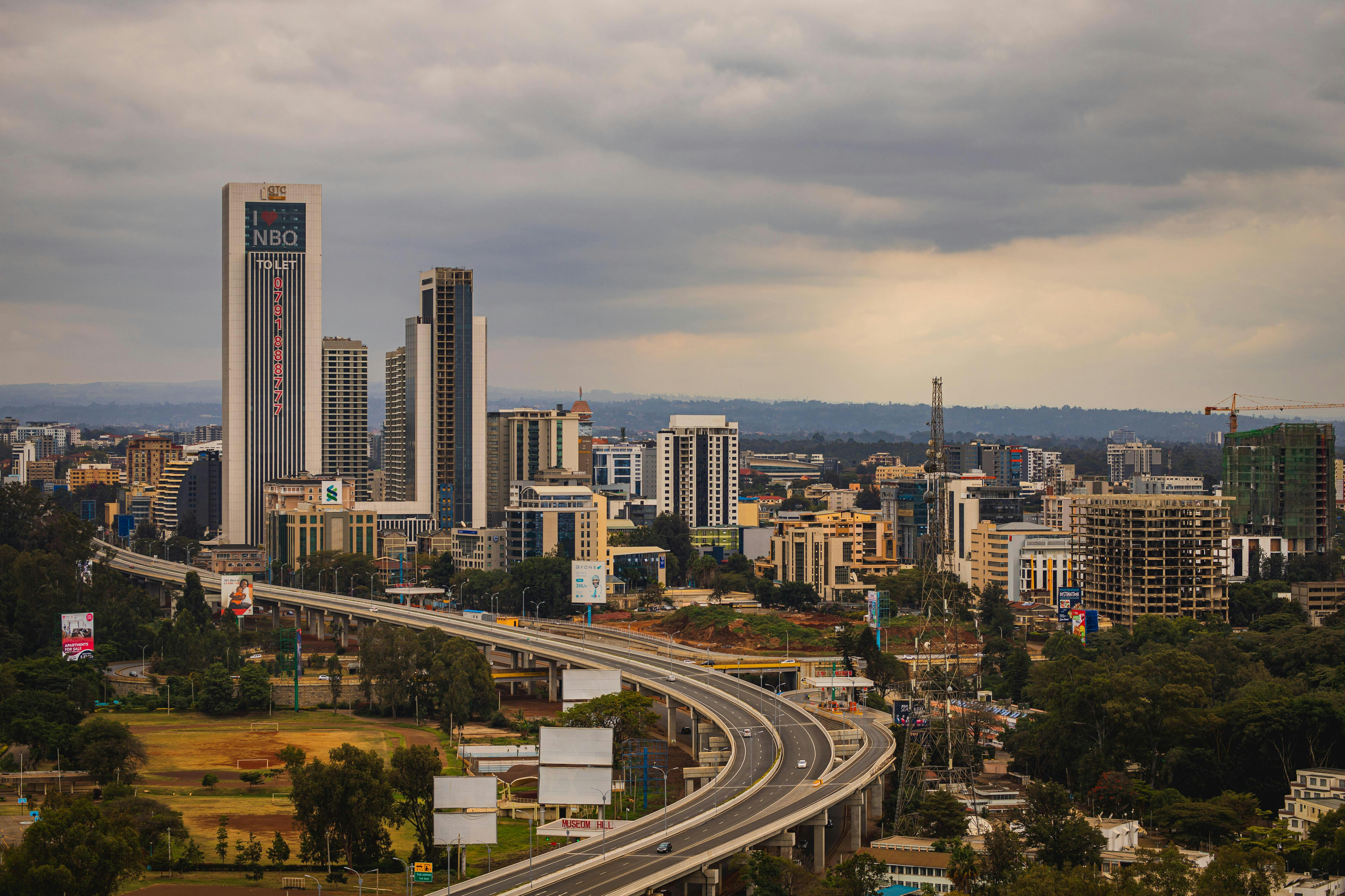 Aerial view of Nairobi's modern skyline and expressway under cloudy skies.