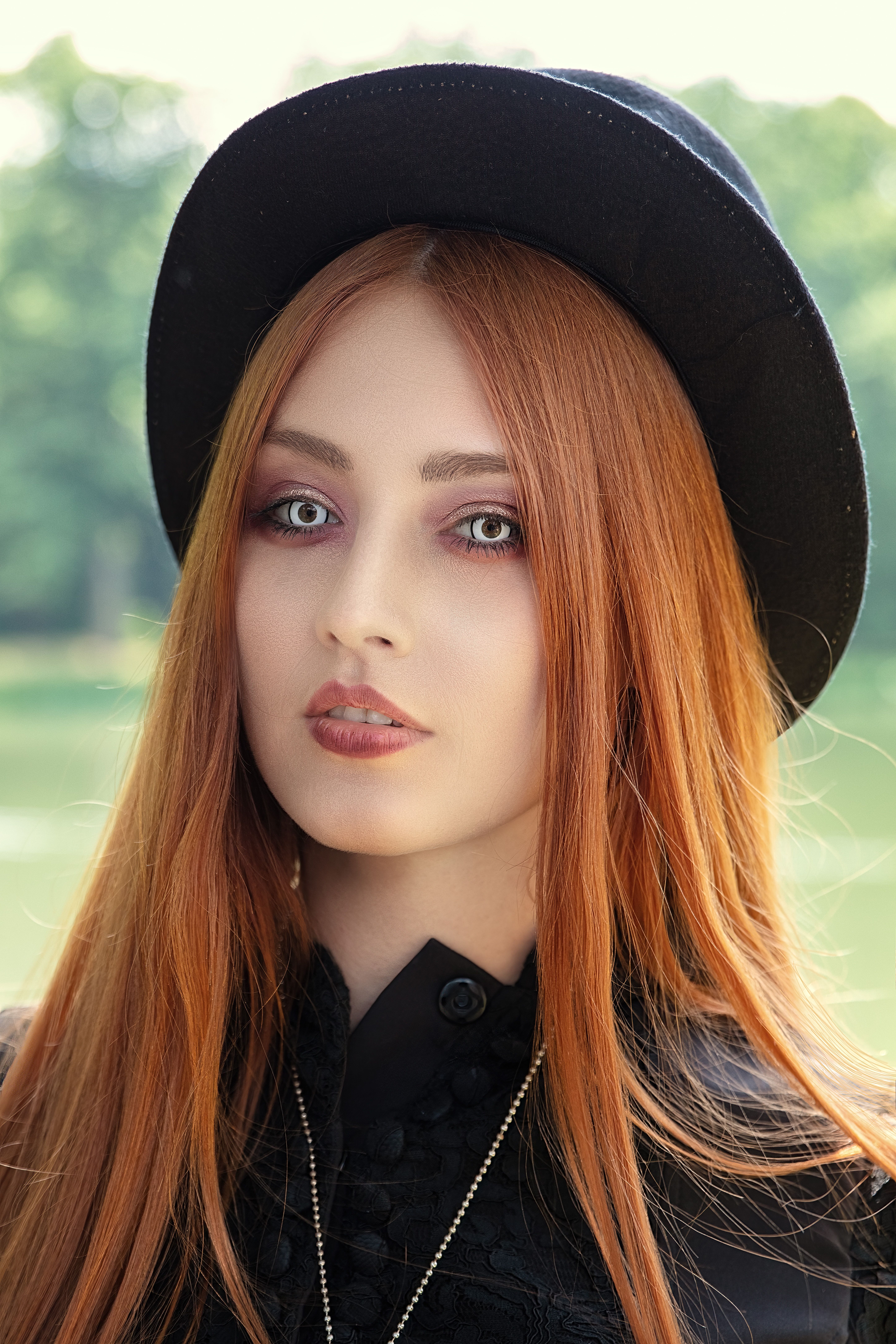 Stylish outdoor portrait of a young woman with red hair and hat in natural light.