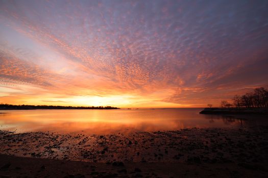 Captivating sunset over a tranquil coast, reflecting vibrant hues on the calm sea.