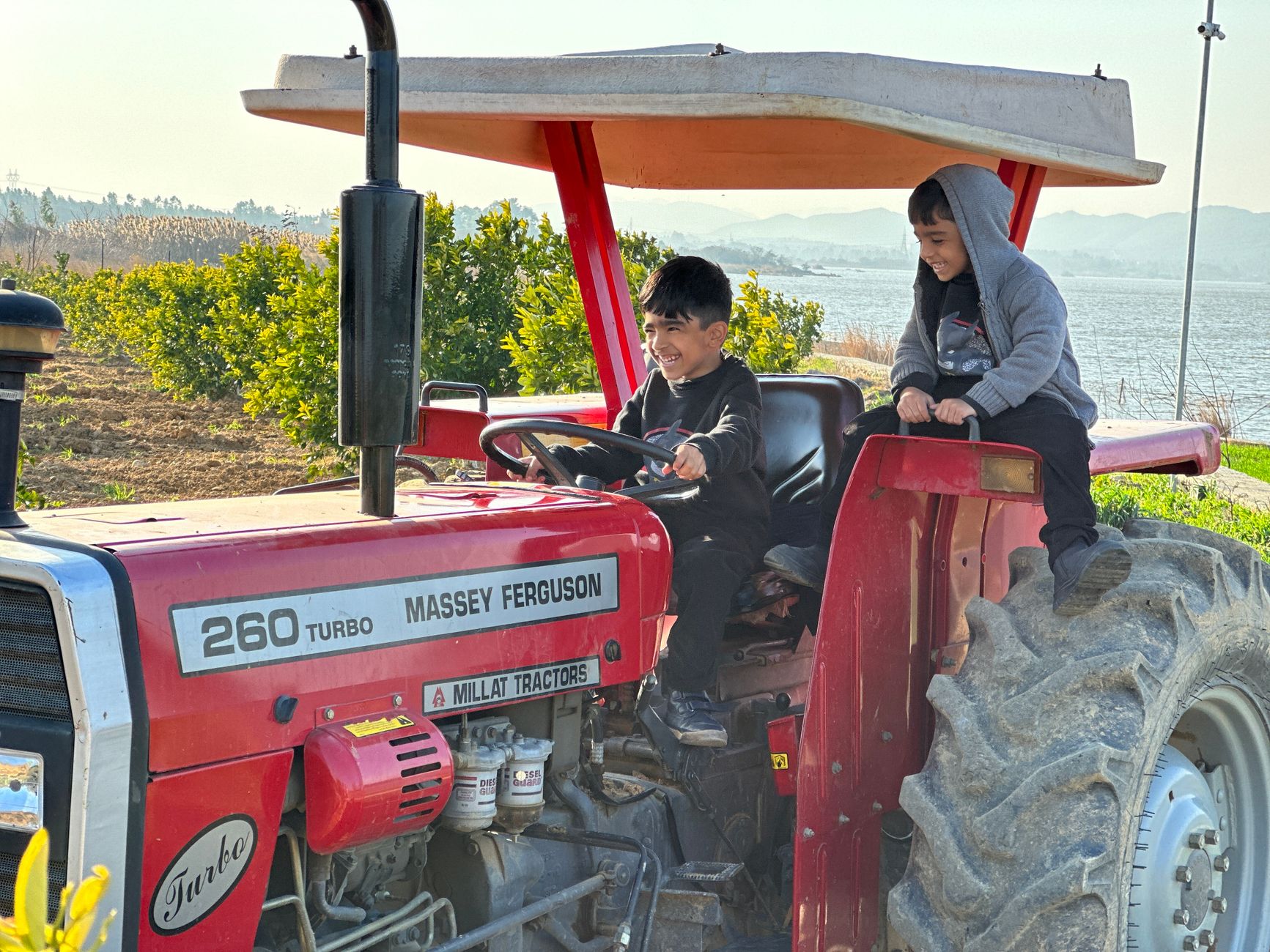 Two happy boys sitting on a red tractor in a rural landscape in Punjab, enjoying the sunny day.