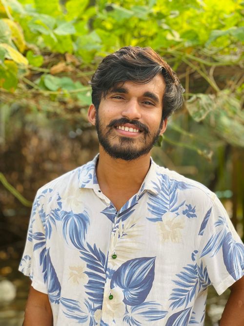 Free Portrait of a smiling young man with black hair in a tropical shirt, outdoors in a lush setting. Stock Photo
