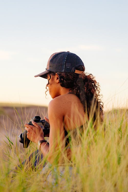 Woman in Cap Sitting with Camera on Grassland