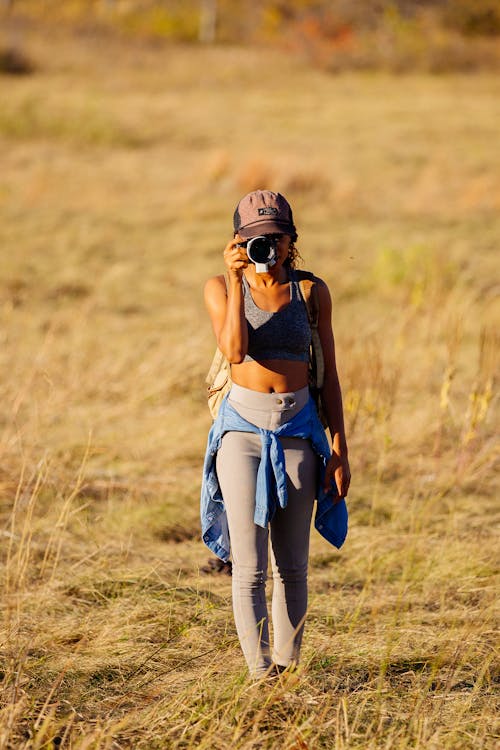 Woman in Cap Taking Pictures with Camera on Grassland