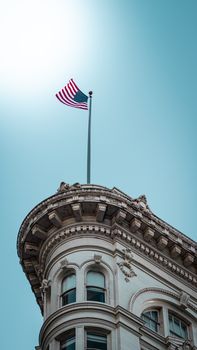 Low angle view of American flag on a classic architectural building against a clear blue sky.