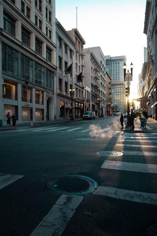 Free Serene urban city street scene at sunset with pedestrians and shadowy tall buildings. Stock Photo