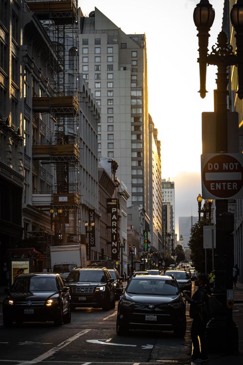 Free City street scene at dusk with cars and tall buildings, showcasing urban life and architecture. Stock Photo