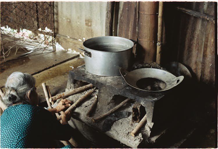 Elderly Woman Cooking On Old Stove In Village