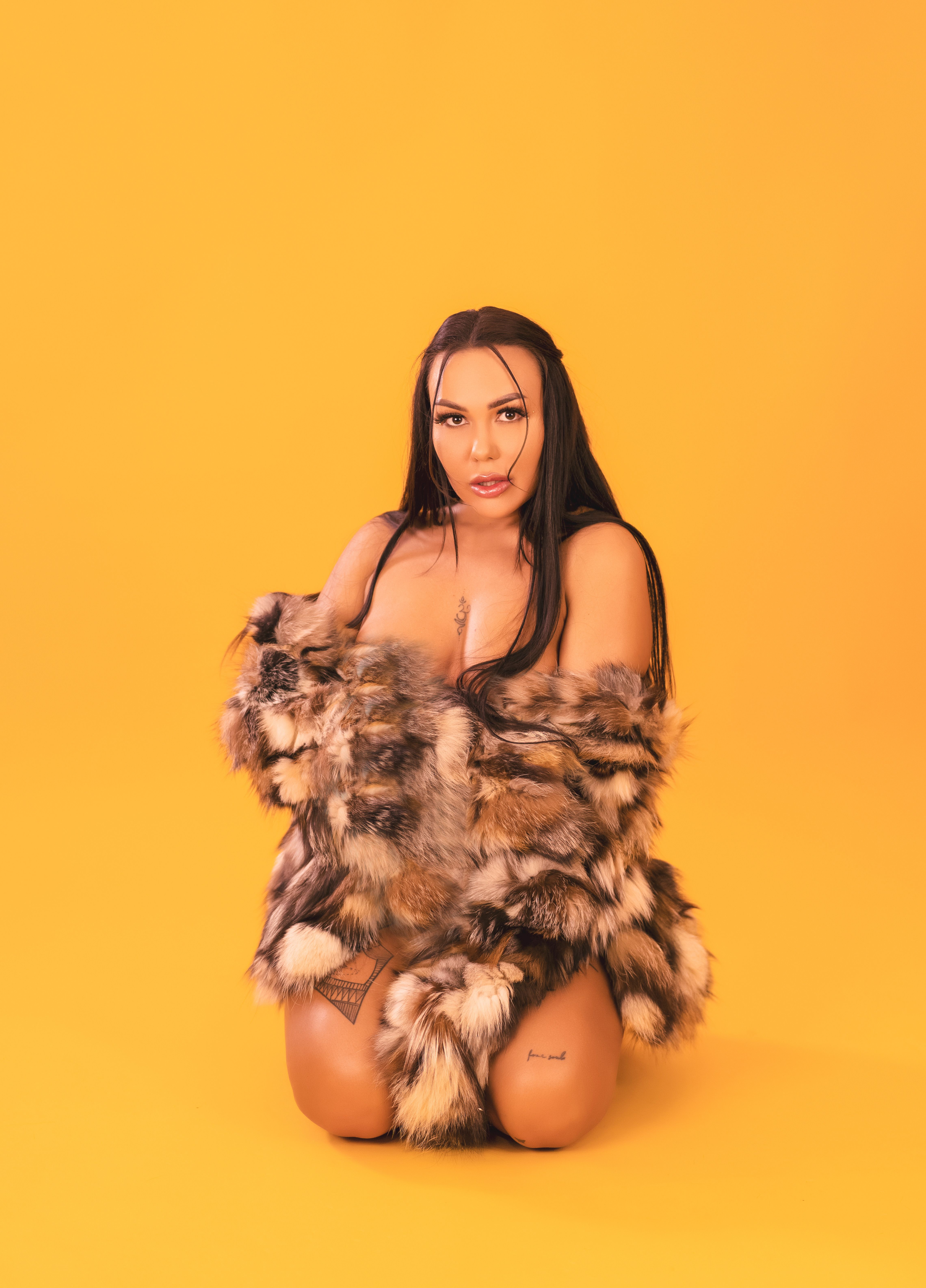Brunette woman posing in fur coat with yellow backdrop, conveying elegance and fashion.
