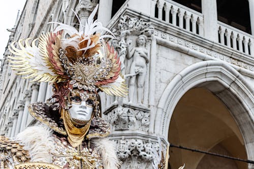 Person in Decorated Mask with Sculptures on Wall behind