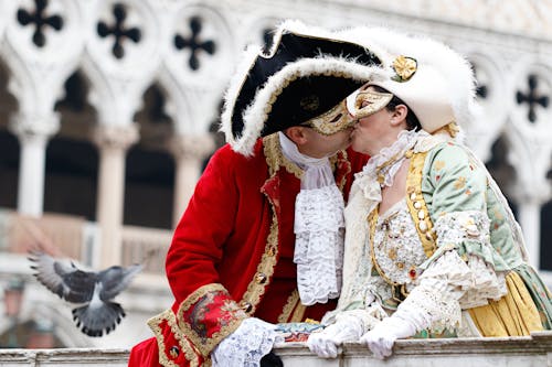 Woman and Man in Costumes with Masks Kissing near Landing Pigeon